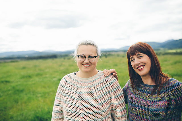 Two women smiling in field wearing crocheted sweaters