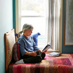 Woman in knitted sweater drinking coffee and reading book on bed