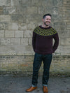 Smiling man wearing bown crocheted sweater in from of stone wall
