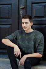Young man sitting on stairs in front of door wearing knitted sweater